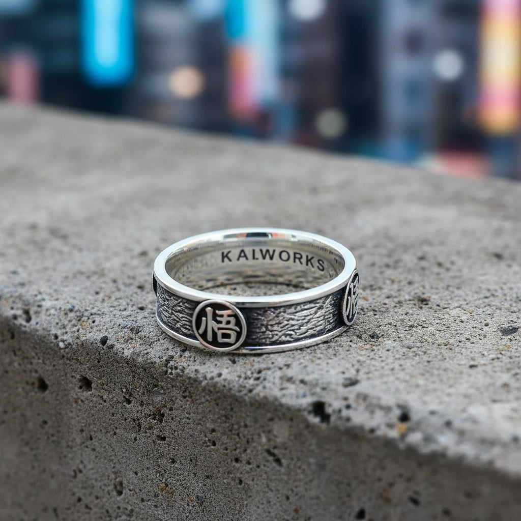A silver ring with engraved Kanji characters on its surface, displayed against a colorful textured background resembling a natural scene.
