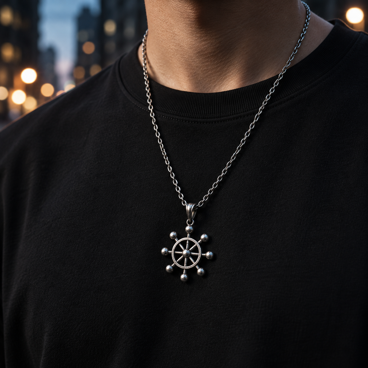 Person wearing a black t-shirt with a silver necklace featuring a wheel pendant, blurred city street in the background.