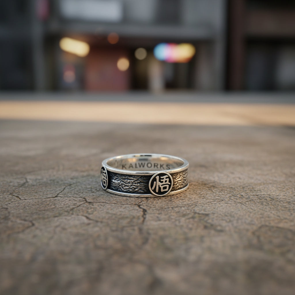 A stainless steel ring with a polished finish, featuring the engraved text 'KAIWORKS' and a four-sided design resembling a Kanji symbol, displayed on a textured dark background.