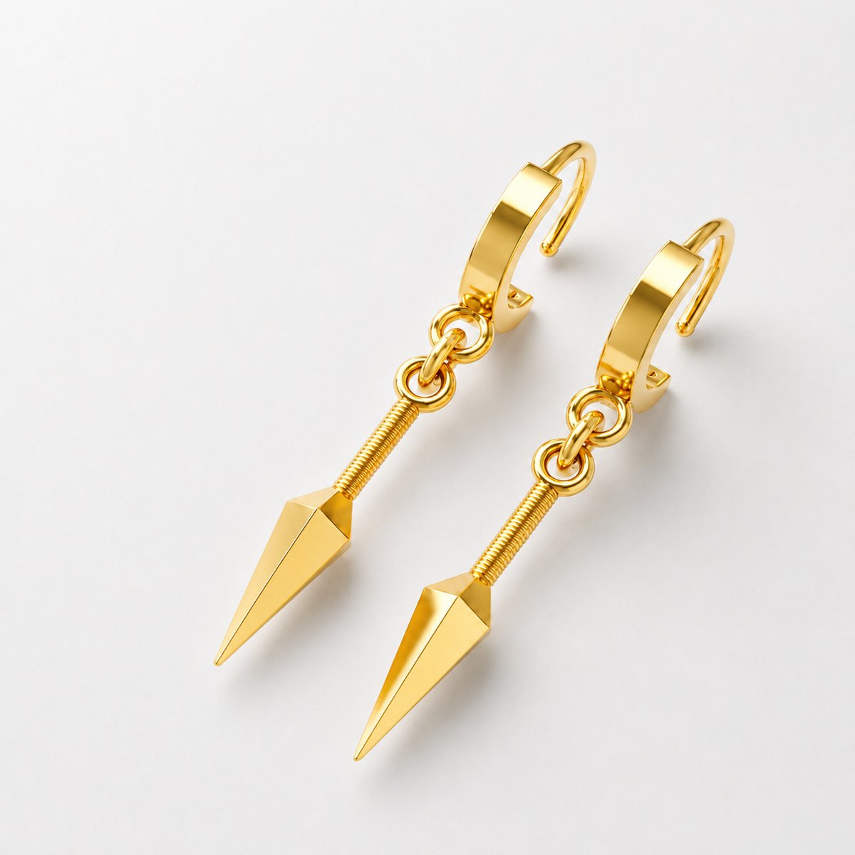 A pair of 14K gold kunai earrings with a polished silver and 18K yellow gold plating, displayed on a wooden surface with a plant in the background.