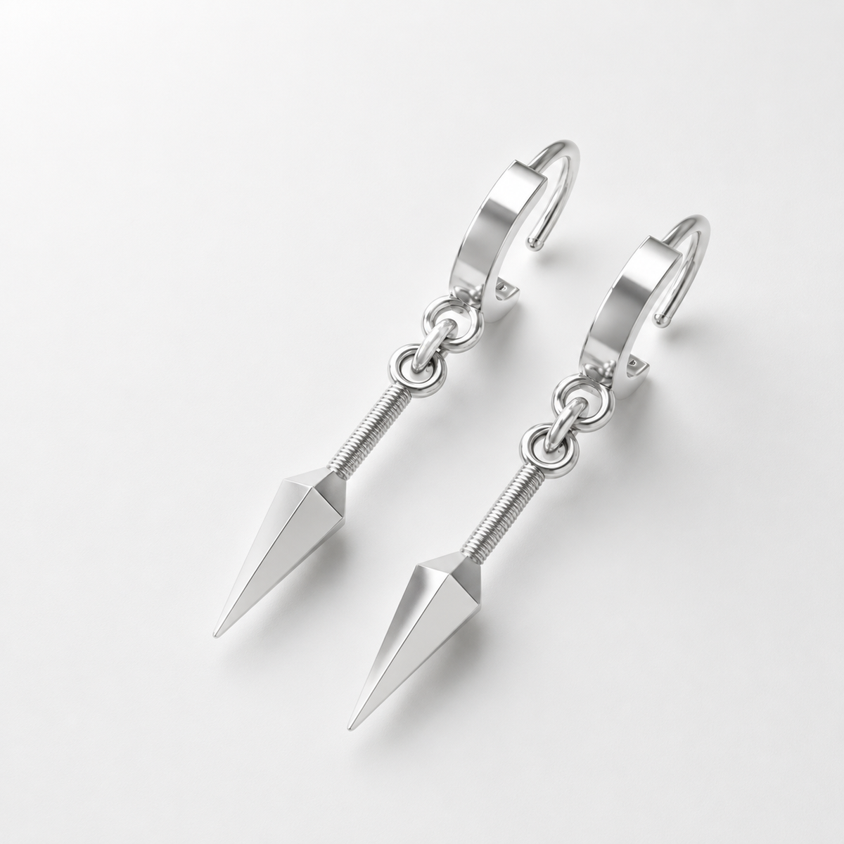 A pair of 14K gold kunai earrings with a polished silver and 18K yellow gold plating, displayed on a wooden surface with a plant in the background.