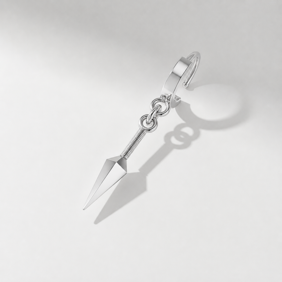 A pair of 14K gold kunai earrings with a polished silver and 18K yellow gold plating, displayed on a wooden surface with a plant in the background.