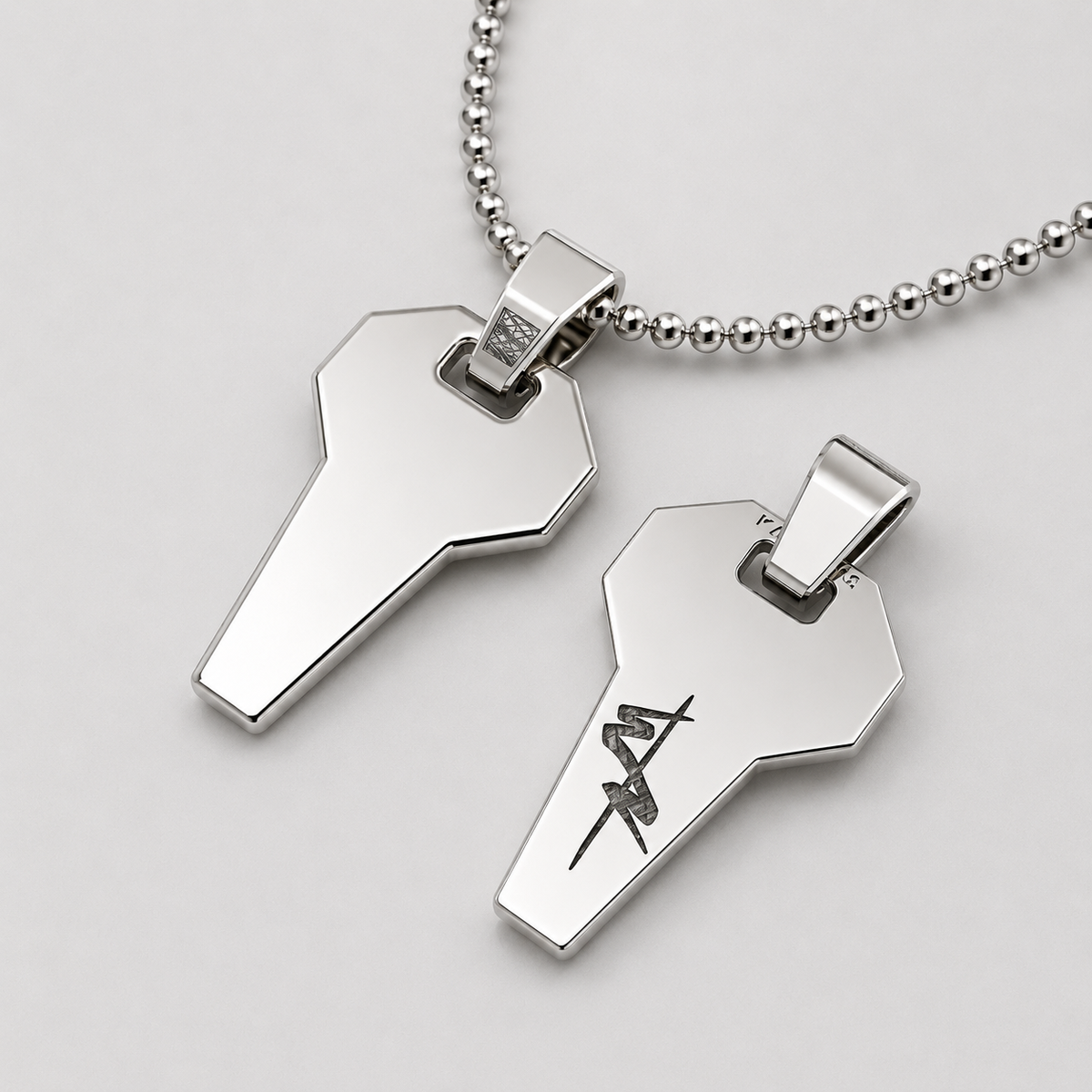 Silver key-shaped pendant on a chain with engraved design on a light gray background