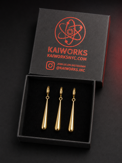 Three gold teardrop-shaped earrings displayed in an open black presentation box with a branded lid. The lid shows the brand name KAIWORKS and social media text in red.
