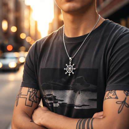 Man wearing a dark t-shirt with a graphic design and a necklace with a pendant, standing on a street.
