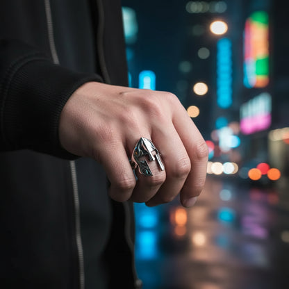 Metallic mask-shaped object held between fingers with 'MASK' text above on a gray background