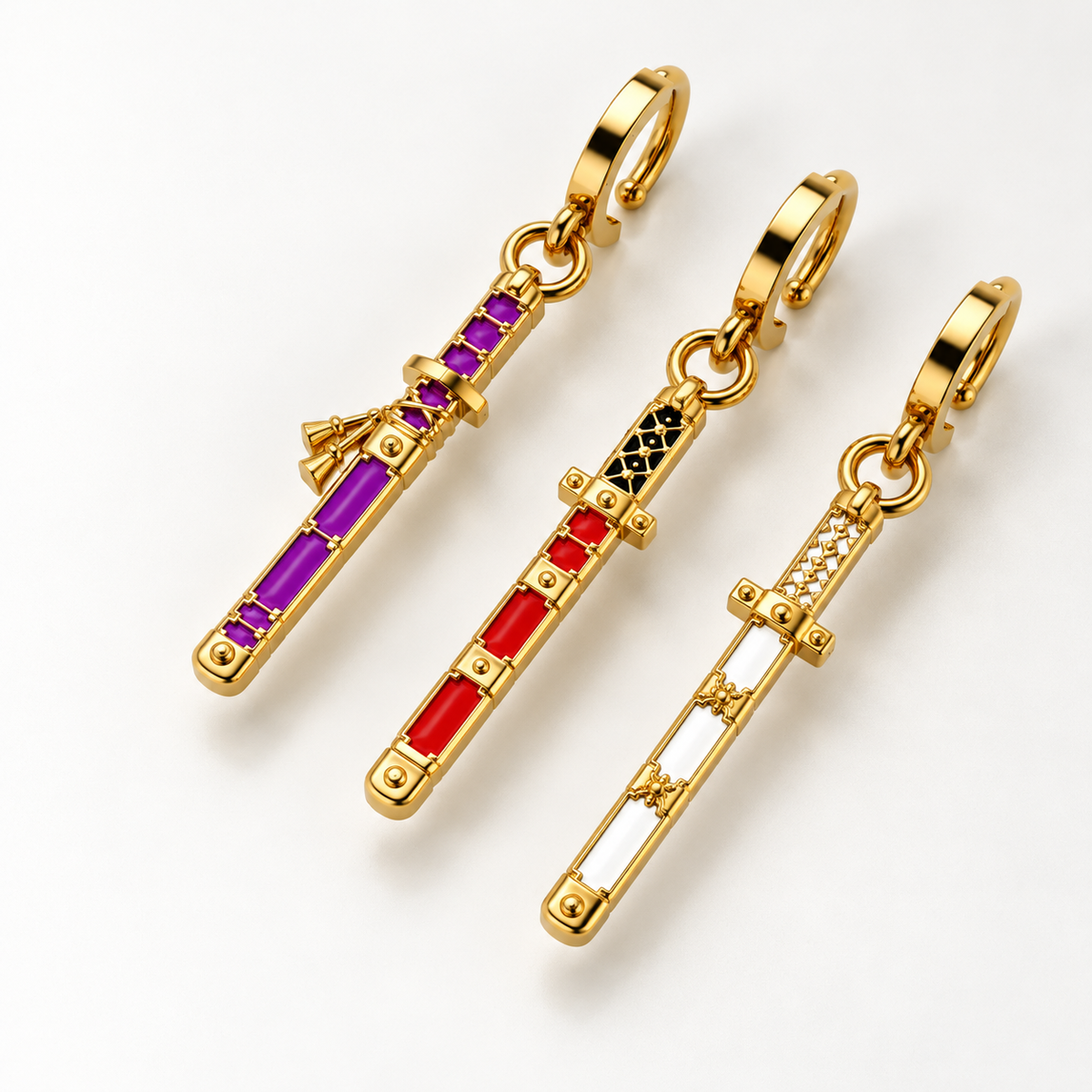 Three gold-tone sword charms with colorful gemstone accents are displayed on a clean white background. The left charm features purple and magenta stones, the middle charm has red and black stones, and the right charm is white and silver.