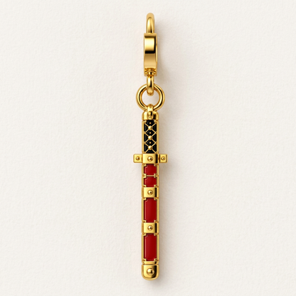 A gold-tone miniature sword charm with red and black enamel details, shown vertically against a clean white background.