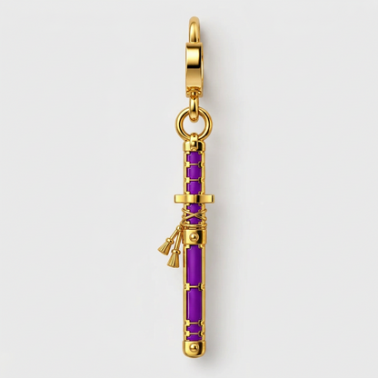 A gold-toned pendant charm shaped like a Japanese sword with vibrant purple inlay details, shown on a light gray background.