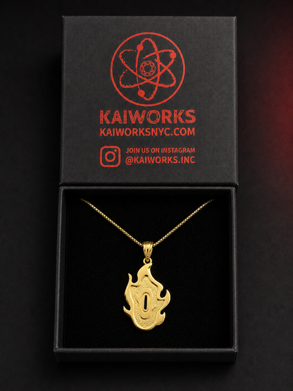 A gold pendant necklace with a flame-like design is displayed inside an open black presentation box. The box lid features the red KaiWorks logo and branding.