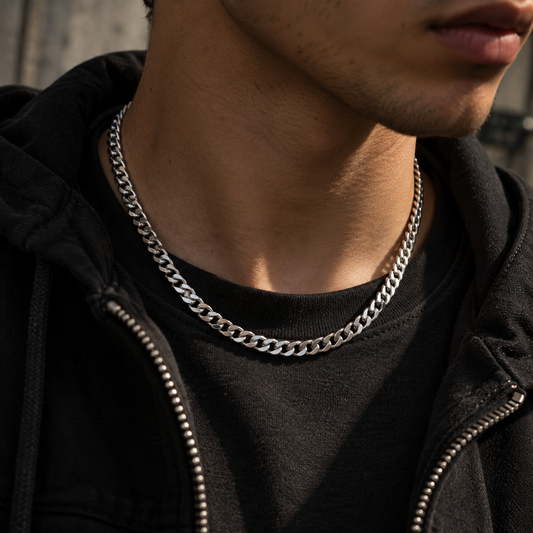 A close-up of a person wearing a thick silver chain necklace over a black t-shirt and black zip-up hoodie.