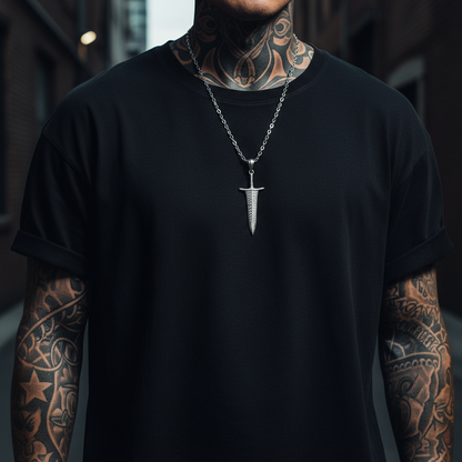 Person wearing a black t-shirt with a silver necklace featuring a unique pendant, standing against a blurred background.