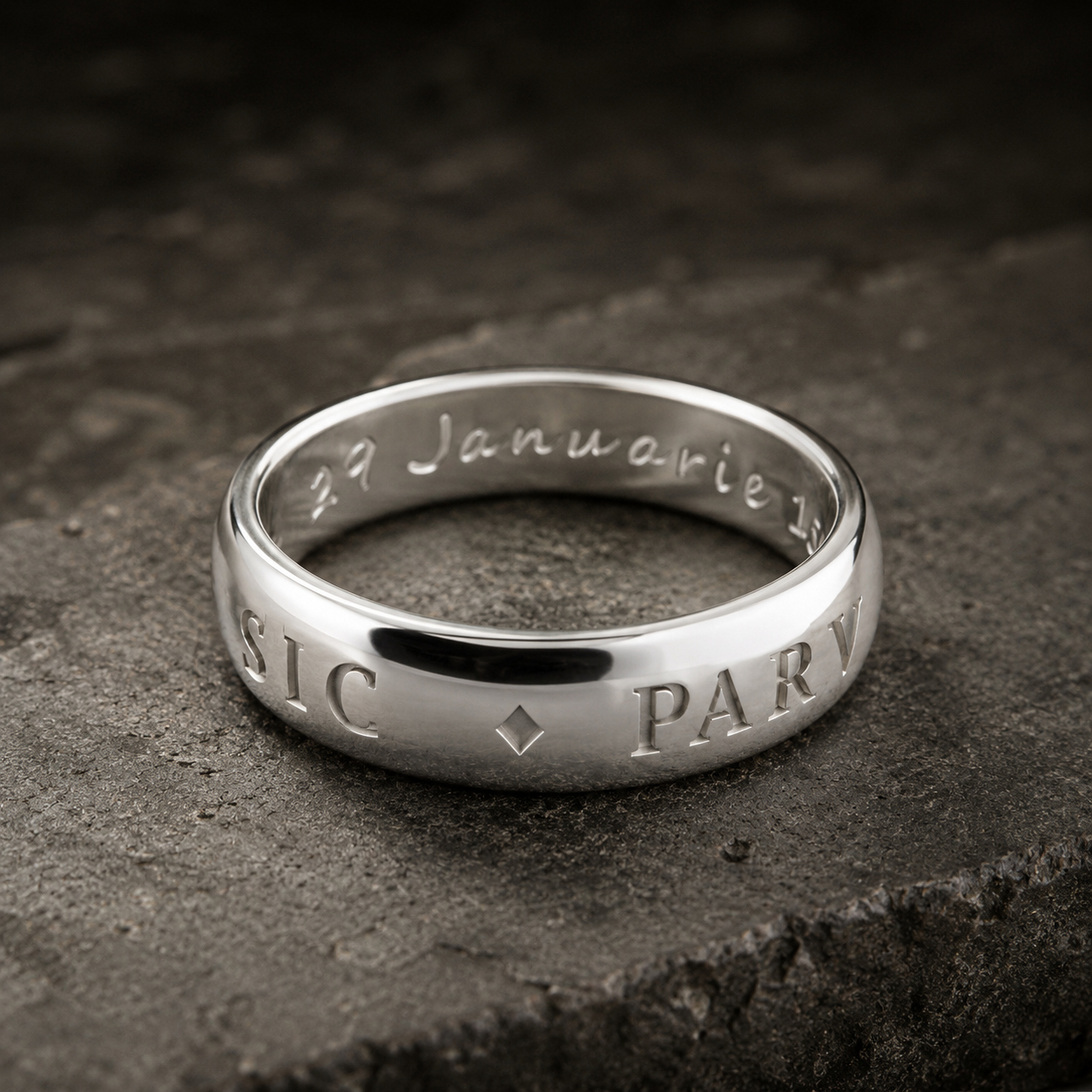 Silver ring with engraved text on a dark stone surface