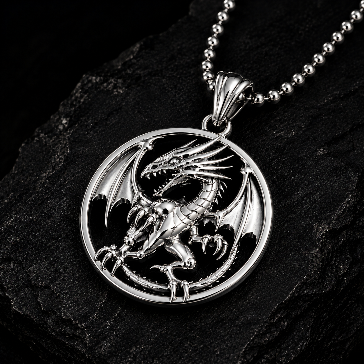 A silver dragon pendant necklace with a detailed circular dragon design, resting on a dark textured rock surface.
